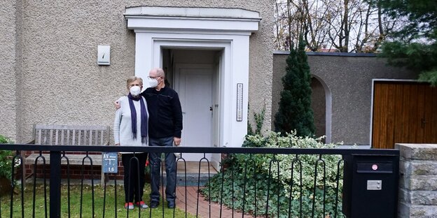Zwei Menschen mit Maske vor einem Haus