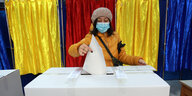 Eine Frau mit Mund-Nasenbedeckung wirft einen Wahlzettel in eine Wahlurne