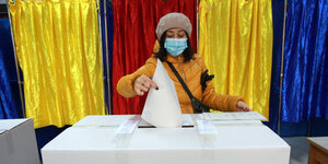 Eine Frau mit Mund-Nasenbedeckung wirft einen Wahlzettel in eine Wahlurne