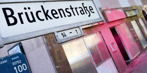Straßenschild „Brückenstraße“ mit pink bemalter hausfront im Hintergrund