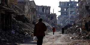 Menschen gehen an beschädigten Gebäuden im palästinensischen Flüchtlingslager Yarmouk am südlichen Stadtrand von Damaskus vorbei