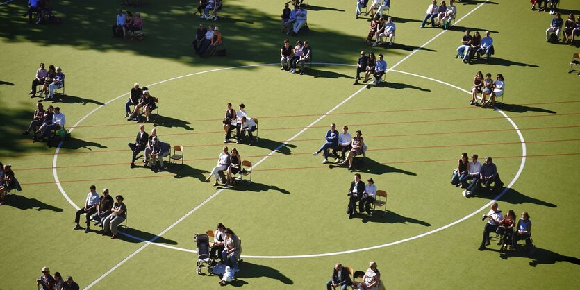 Familien mit Abiturient*innen sitzen auf einem Sportplatz