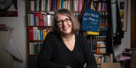 Verlgerin Britta Jürgs sitzt auf einem Stuhl vor einer Bücherwand