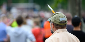 Mann trägt ein Kappe mit Spritze im Kopf