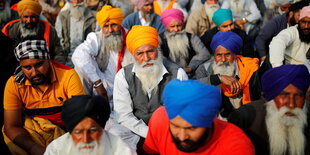 Männer mit Turban sitzen auf dem Boden und lauschen einem Redner