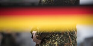 in Soldat zeichnet sich hinter einer schwarz-rot-goldenen Banderole ab