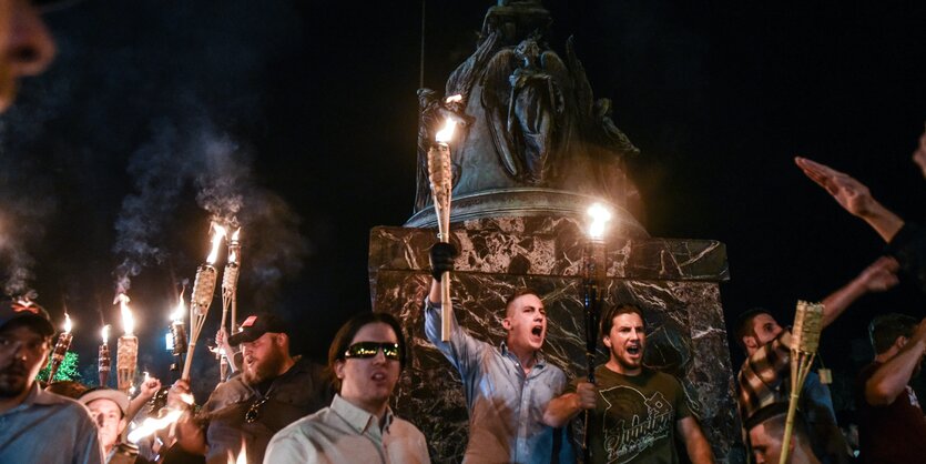 Fackeltragende schreiende Männer vor einem Denkmal in der Nacht