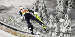 Skispringer in der Luft, im Hintergrund Schneelandschaft