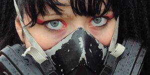 Eine stark geschminkte junge Frau mit einem Mund-Nasen-Schutz aus Metall.