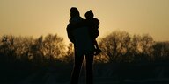 Mutter mit Kind auf dem Arm betrachtet den Sonnenuntergang