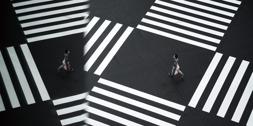 Ein Mann mit Maske geht über einen Zebrastreifen