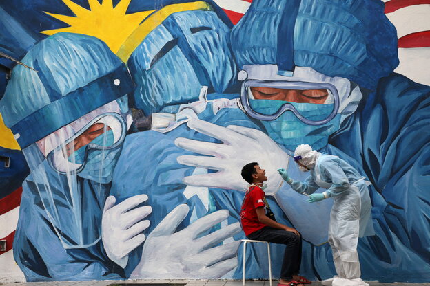 Ein Arzt führt einen Coronatest bei einem jungen Mann vor einer Graffiti Wand auf der sicj Ärtze umarmen, durch