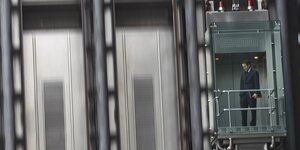 ein Banker fährt im gläsernen Aufzug am Llloyd's Building London