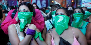 Mehrere Frauen mit grünen Halstüchern vor dem Gesicht halten sich die Hände