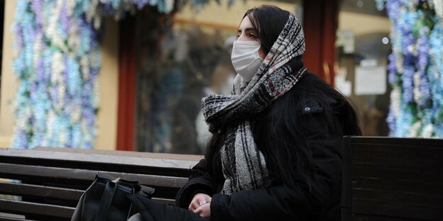 Ein Frau mit Maske sitzt auf einer Bank in der Kälte
