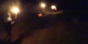 Zwei Kinder in Anorak und mit Mütze tragen brennende Fackeln durch die Nacht. Vor ihnen ist noch eine weitere Fackel, aber es ist nicht erkennbar, wer sie trägt.