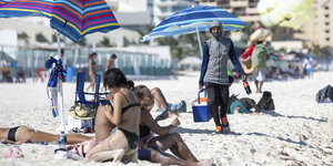 Ein Verkäufer läuft am Strand entlang und bietet Getränke für Touristen an, die in der Sonne liegen