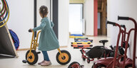 Ein kleines Mädchen mit einem Laufrad steht alleine im Flur einer Kita