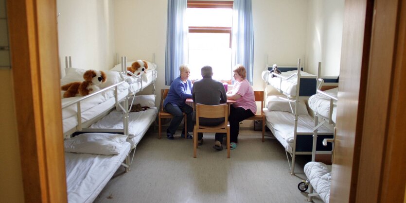 Drei Menschen sitzen an einem Tisch zwischen Stockbetten