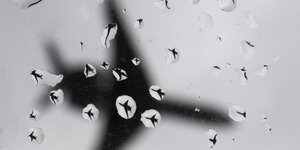 Ein Flugzeug landet am Flughafen Hannover, und spiegelt sich dabei in vielen Regentropfen auf der Windschutzscheibe eines Autos