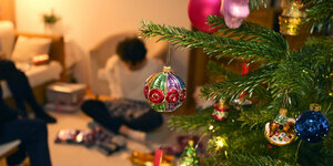 Weihnachtsbaum, im Hintergrund unscharf eine Person, die Geschenke auspackt