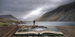 Ein Mann schaut auf einen großen See - der See spiegelt sich in einem im Vordergrung liegenden Buch