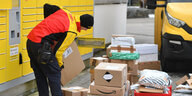 DHL-Paketbote entlaedt sein Postauto und legt Pakete in Fächer einer Packstation