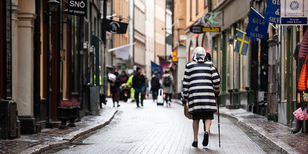 Eine alte Frau mit Stock läuft durch die Altstadt von Stockholm