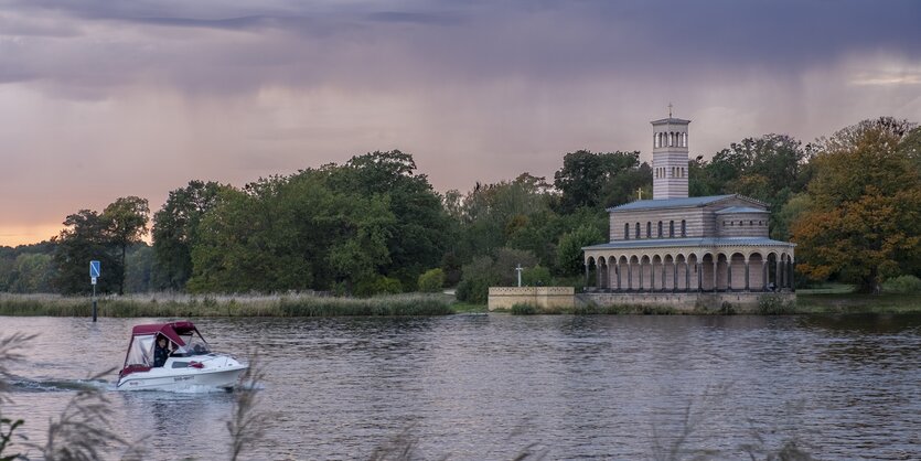 Ein kleines Motorboot fährt an der direkt an der Havel gebauten Heilandskirche vorbei.