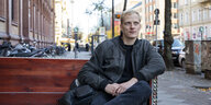 Der Schriftsteller Lorenz Just hat sich während eines Spaziergangs mit Interview auf eine Bank gesetzt und blickt in die Kamera