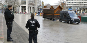 Das Bild zeigt zwei Polizisten, die beobachten, wie eine Bretterbude, offenbar für Glühwein, abtransportiert wird.