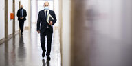Finanzminister Olaf Scholz läuft mit Mund-Nasen-Bedeckung und Unterlagen einen Flur entlang