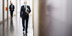Finanzminister Olaf Scholz läuft mit Mund-Nasen-Bedeckung und Unterlagen einen Flur entlang