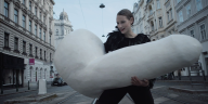 Eine Schauspielerin trägt eine vielfach überdimensionierte Penisskulptur durch die Straße.