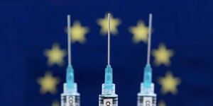 Drei Spritzen mit Coronaimpfstoff vor einer EU Flagge