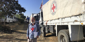 Ein Mitarbeiter des Internationalen Roten Kreuzes vor einem LKW Konvoi