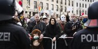 Demonstranten stehen mit und ohne Masken vor einer Absperrung