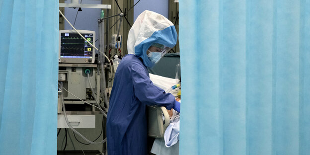 Eine Krankenschwester in Schutzkleidung pflegt einen Patienten auf der Corona-Intensivstation