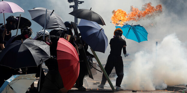 Demonstranten mit Regenschirmen bei Protesten in Hongkong - ein Schirm fängt Feuer