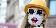 Eine Frau trägt Kleidung im Pop Art Style und eine passende Mund-Nasen-Bedeckung, auf der ein Mund aufgedruckt ist