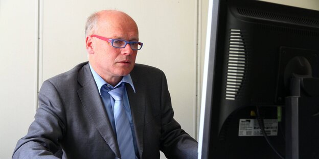 Ein älterer Mann sitzt vor einem Computer. Er trägt eine Brille und hatt schütteres Haar
