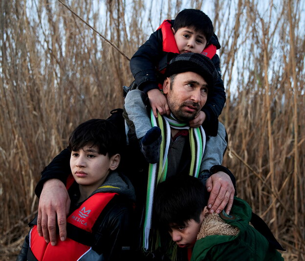 Ein Mann trägt seine drei Kinder, sie sind warm angezogen, weil es im Winter auf Lesbos sehr kalt ist