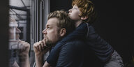Ein Vater trägt seinen Sohn auf dem Rücken und schaut aus dem Fenster