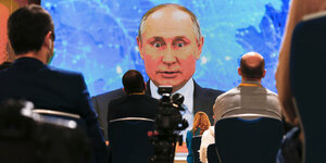 Wladimir Putin auf einer großen Leinwand - davor sitzen Journalisten