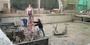 Auf einer Baustelle in einem gekachelten Becken steht eine Frau auf einer Leiter