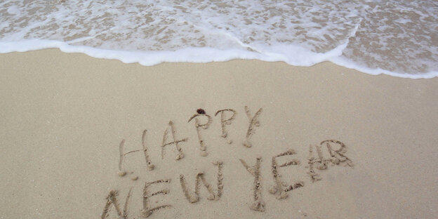 Happy new Year steht an einem Strand in den Sand geschrieben.