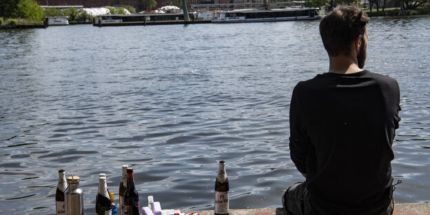 Ein Mann sitzt am Ufer an der Spree - mit ein paar Bierflaschen