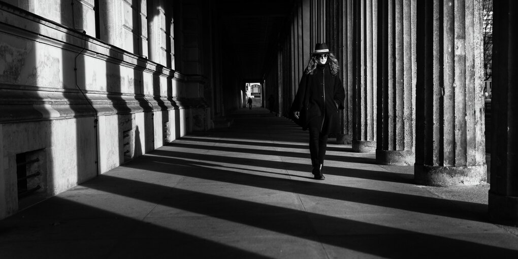 Eine Frau flaniert auf der Museumsinsel in Berlin-Mitte an Säulen vorbei