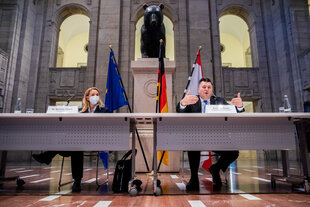 Slowik und Geisel sitzen bei einer Pressekonferenz an einem Tisch in einem großen Saal