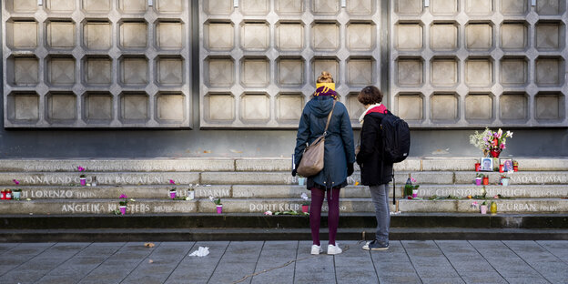 Zwei Menschen stehen vor den Stufen zur Gedächtniskirche, wo 2016 der Anschlag stattfand. Dort stehen die Namen der Opfer auf Stufen, außerdem stehen dort Kerzen